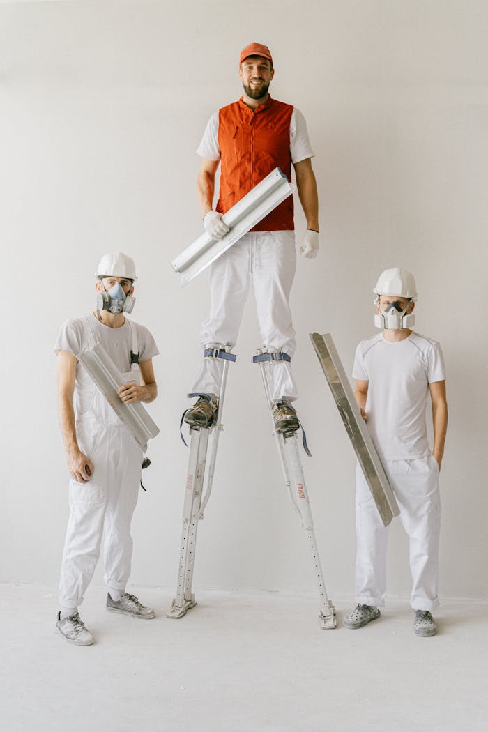 Inicio Construction workers in uniforms and hard hats using drywall stilts indoors.